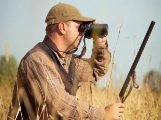 Aficionado observando fauna en campo abierto durante una jornada de caza ética.