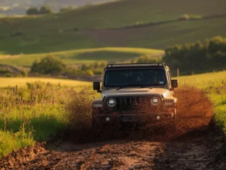 Un vehículo todoterreno cruza una zona de barro levantando salpicaduras de tierra y agua mientras avanza por un camino de campo rodeado de vegetación en un entorno rural.
