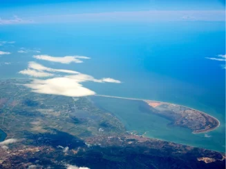 Vista aérea del Delta del Ebro en Tarragona, mostrando la desembocadura del río, los arrozales, la laguna de la Tancada y la barra del Trabucador bajo un cielo azul.