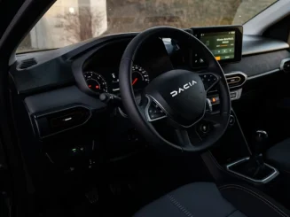 Interior de un coche Dacia, mostrando el volante con el logo de Dacia, el panel de instrumentos y la pantalla central del sistema de infoentretenimiento.