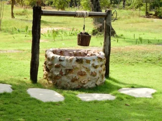 Pozo de agua de piedra en un entorno rural, con cuerda y cubo colgando.